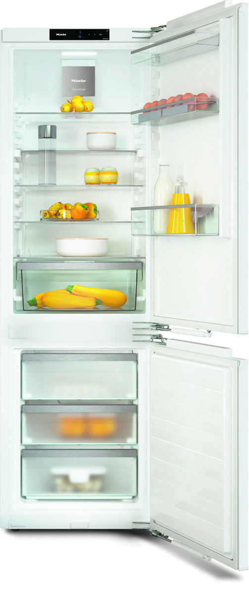 Open white Miele refrigerator, shelves holding lemons, eggs, milk, juice, yellow squash, and fruits; freezer drawers below.