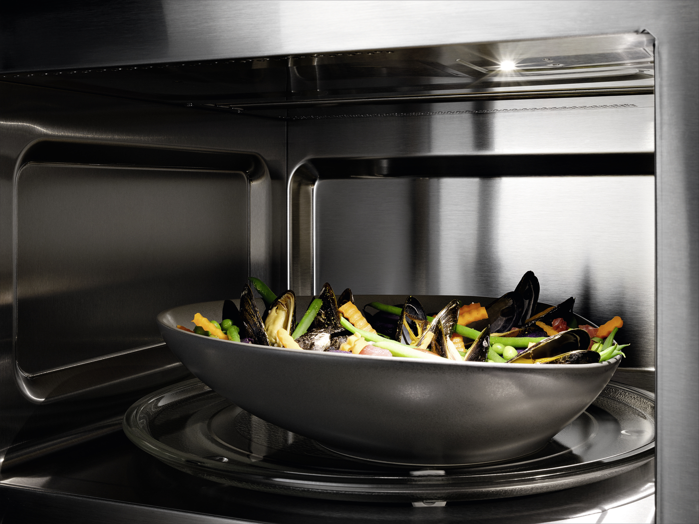 A stainless steel microwave oven with a gray bowl of mussels, carrots, and green beans inside, ready to heat.
