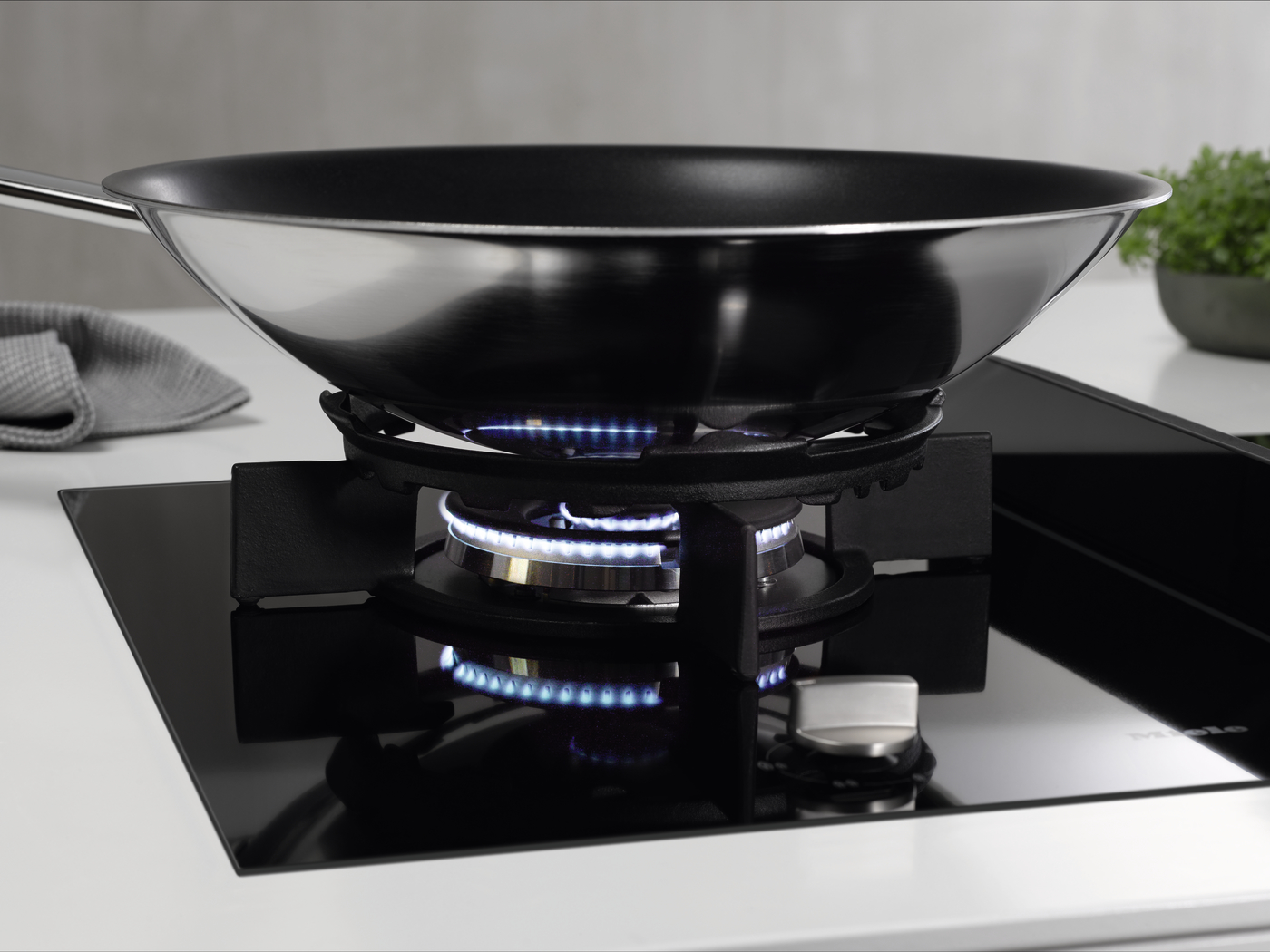Stainless steel frying pan on a lit gas stove with blue flames beneath the pan.