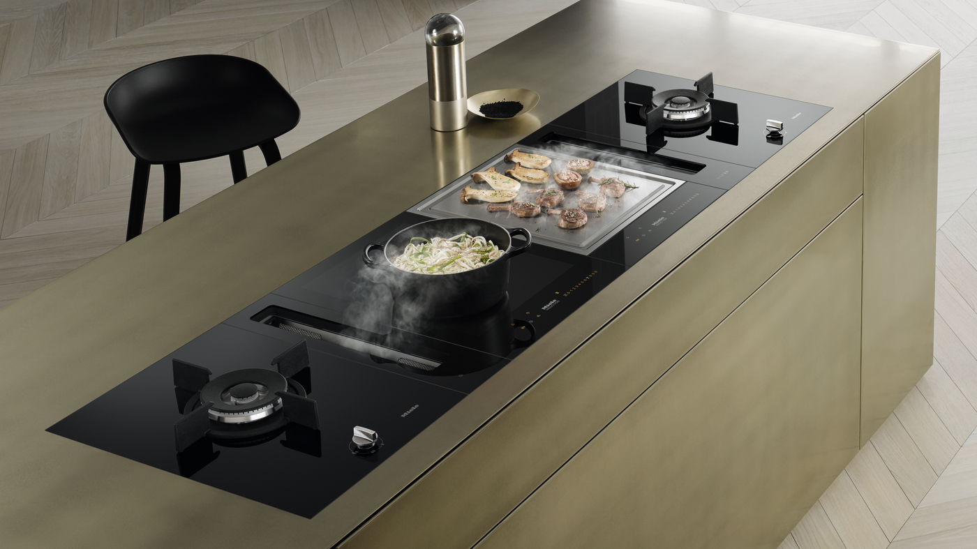 Modern kitchen island with two gas burners, a built-in grill, and a hot pan of steaming pasta on the counter-top grill surface.