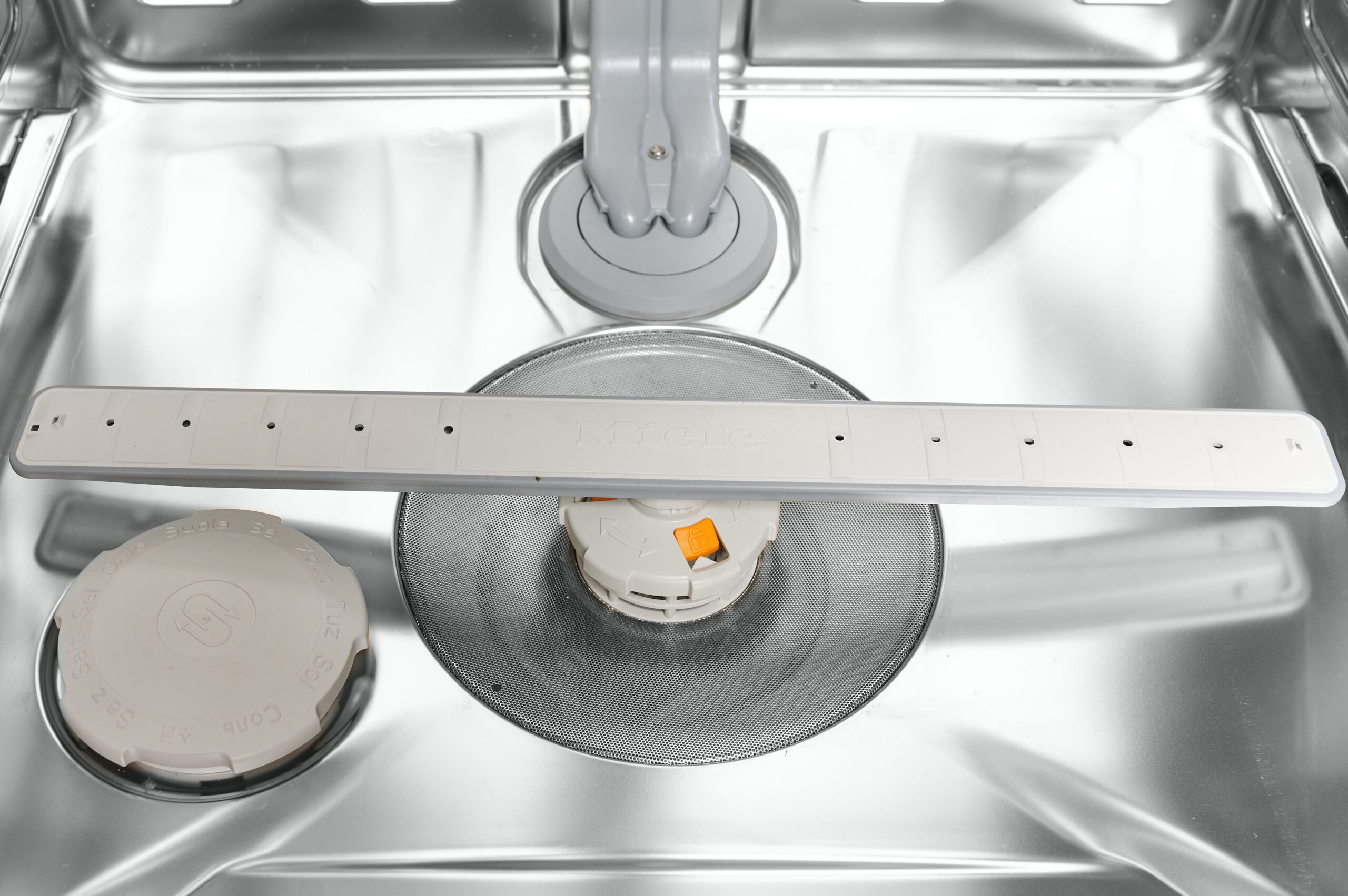 Inside view of a stainless steel dishwasher tub with a central circular spray arm hub and surrounding racks used for washing dishes