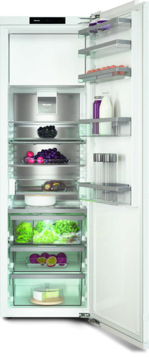Open modern refrigerator with glass shelves filled with produce (grapes, leafy greens, citrus), dairy (milk), juice bottles, and a cake on the bottom shelf, all neatly organized.