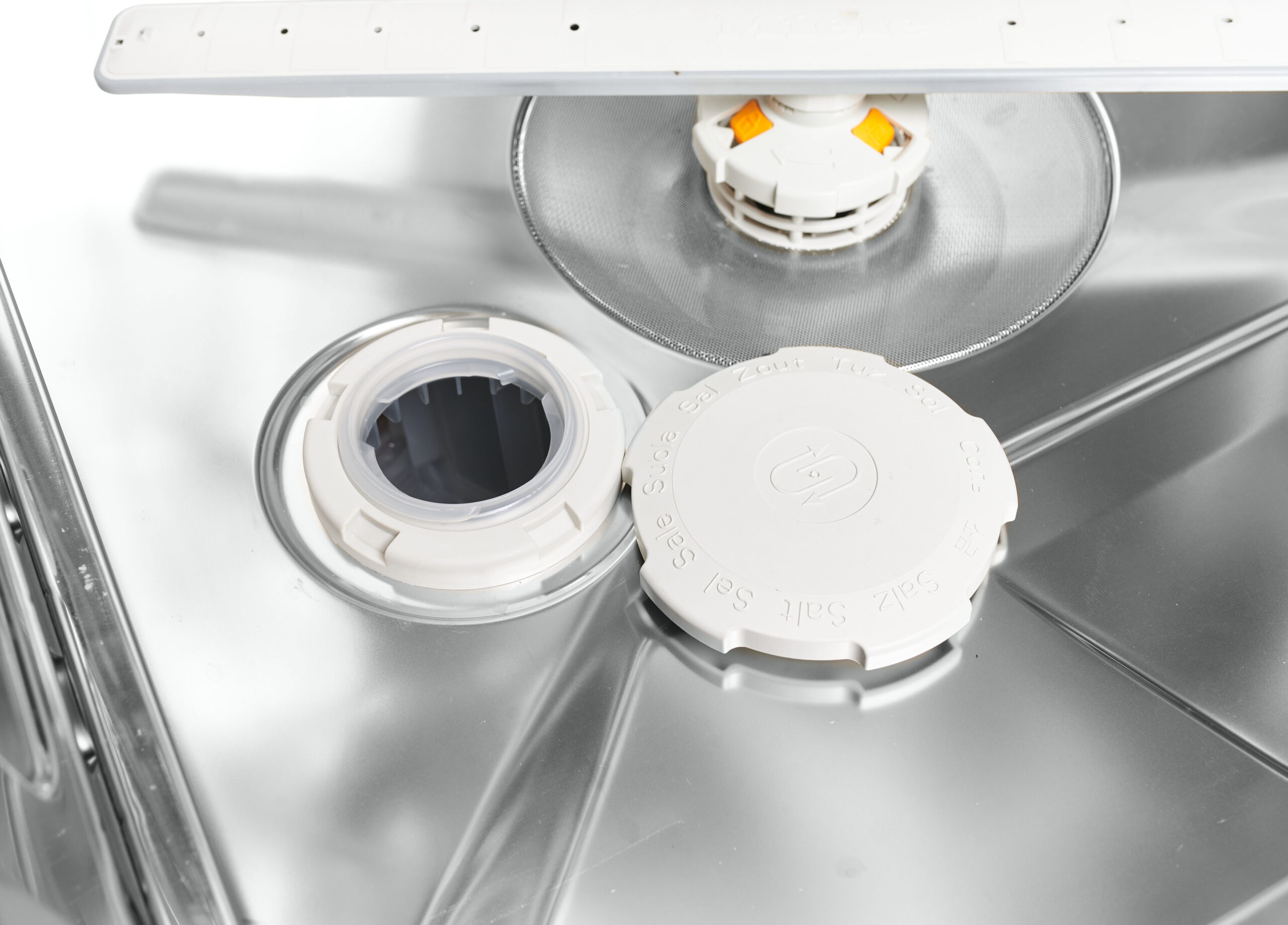 Close-up of a washing machine drum area with detergent cap and circular inlet compartments visible inside a stainless steel tub.
