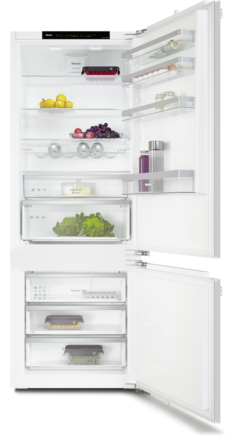 Open white refrigerator with fruits and vegetables on shelves and in drawers; bottom freezer with multiple trays clsd by door shelves with bottles nearby.