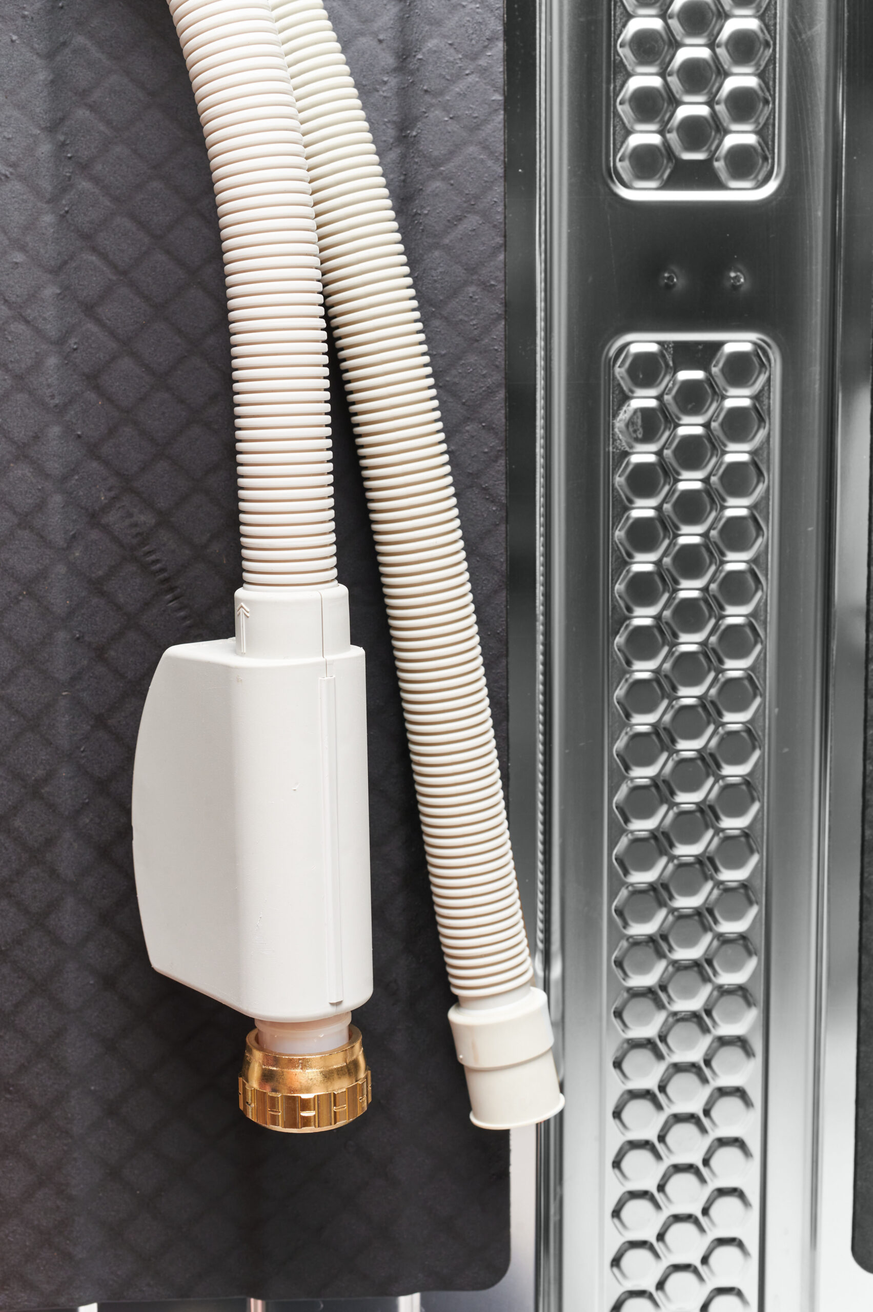Two white flexible hoses with a plastic connector sit on dark padded surface beside a metal honeycomb vent panel.