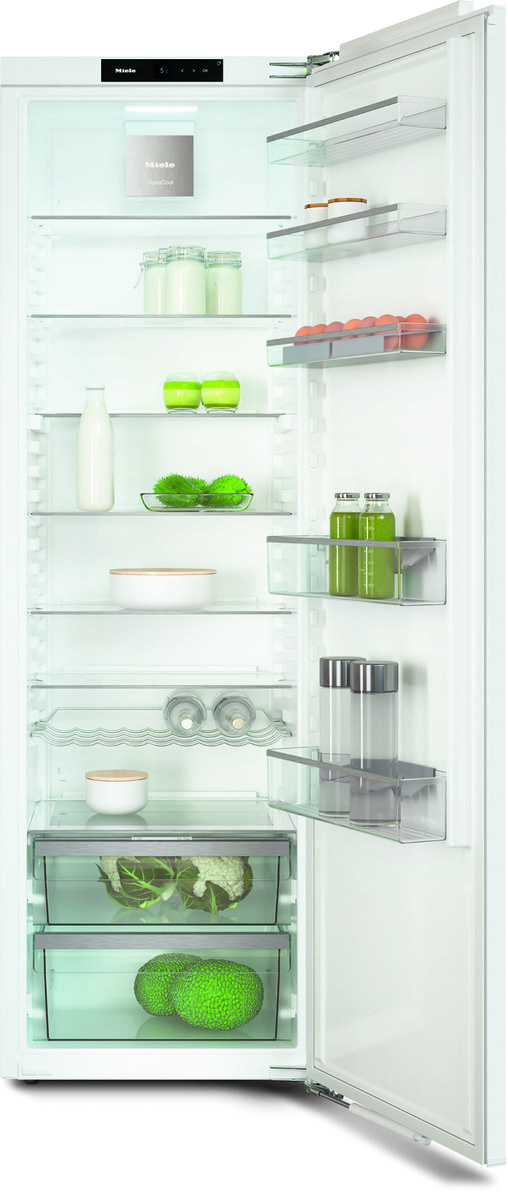Open white refrigerator showing shelves with milk, jars, eggs on the door, and leafy greens in the lower drawers.