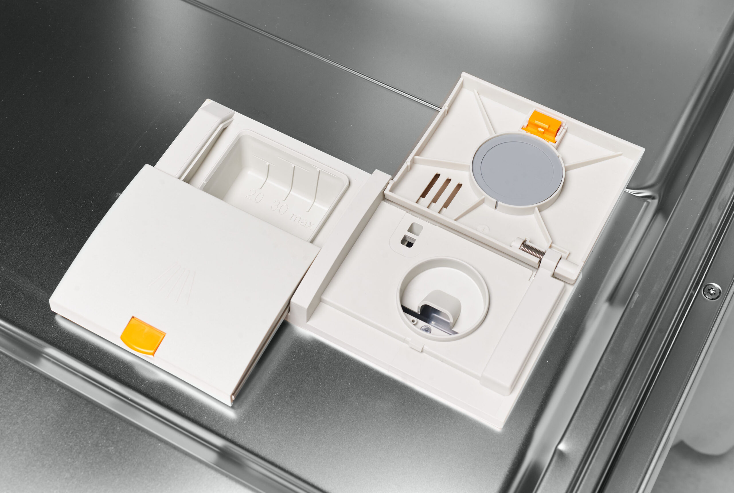 Open dishwasher detergent compartment with a gray circular cap and orange latch, shown in the door.