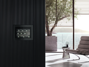 Modern spa-like living room with a built-in wine cooler set in a dark ribbed wall, overlooking a sunny ocean view.
