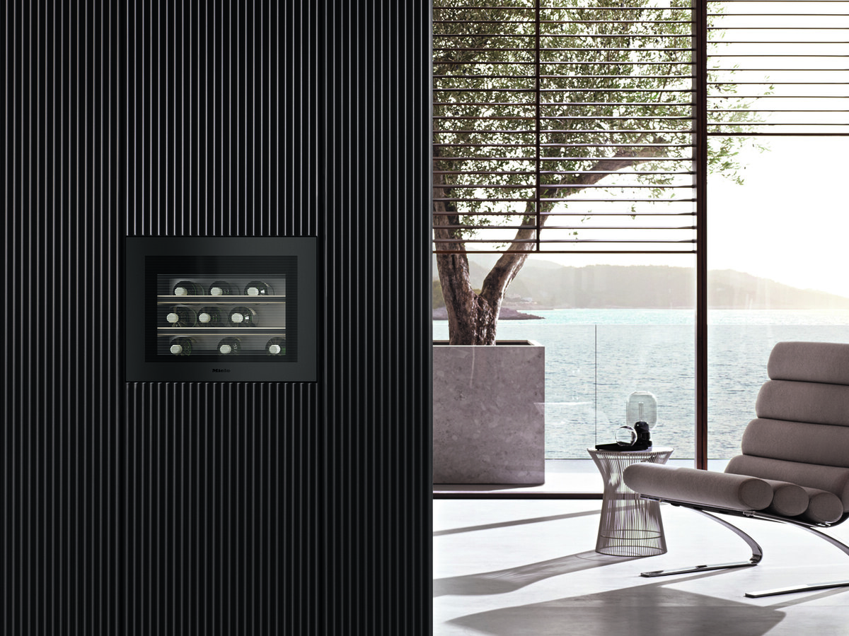 Modern spa-like living room with a built-in wine cooler set in a dark ribbed wall, overlooking a sunny ocean view.