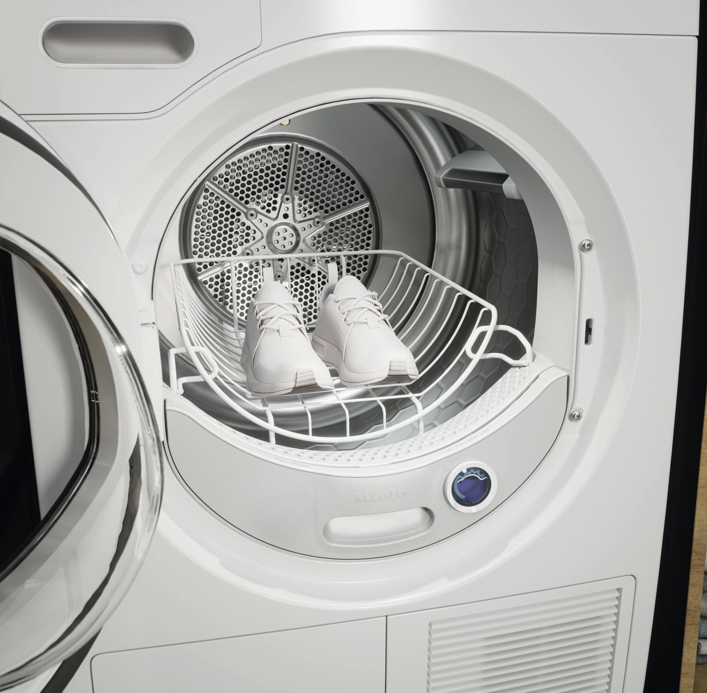 White sneakers resting on a drying rack inside a front-loading clothes dryer.