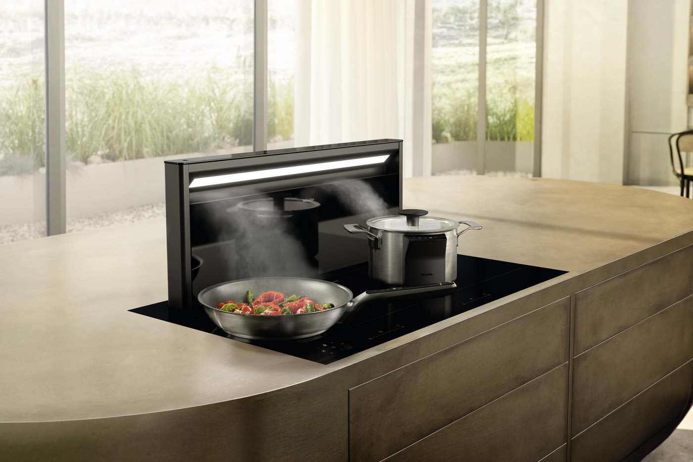 Modern kitchen island with a black induction cooktop, a stainless wok filled with peppers and greens, and a steaming stainless pressure cooker nearby.