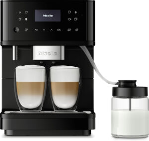 Front view of a black Miele coffee machine brewing two cappuccinos in clear glass cups with a milk jug on the side.