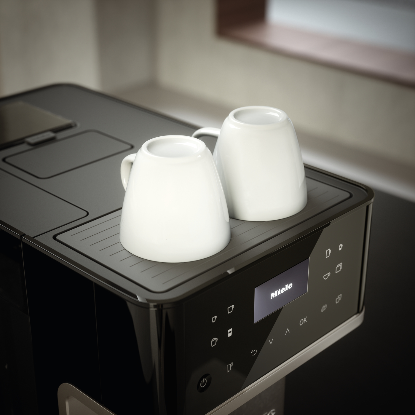 Two white ceramic mugs resting upside down on the top of a black Miele coffee machine.