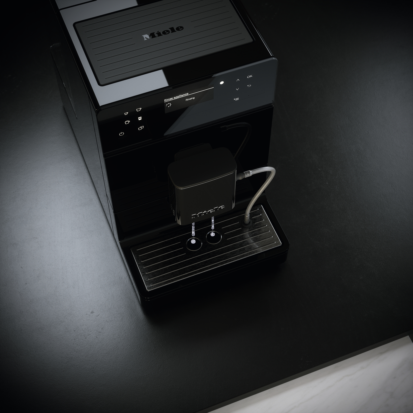 Miele espresso machine on a dark countertop with a portafilter and metal drip tray nearby.