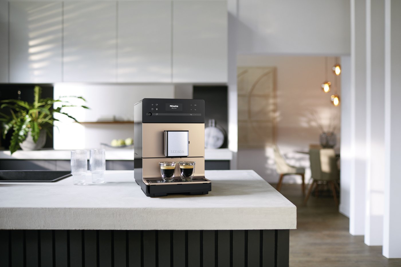 Miele coffee machine on a kitchen island dispensing two espresso shots into small glass cups.