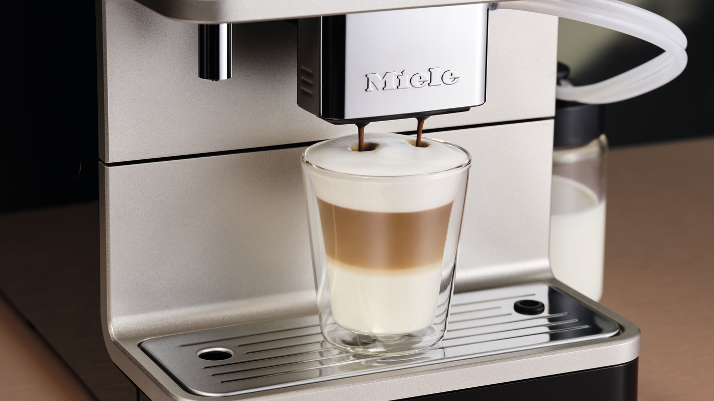Espresso machine pouring a layered latte into a glass, with 'Miele' branding visible on the machine.