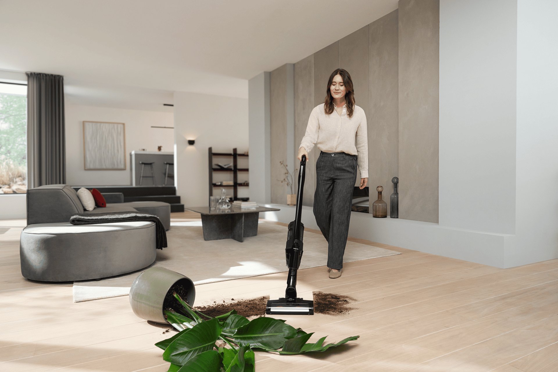 Woman in a beige blouse vacuums a mess of soil and plant leaves spilled from a toppled pot in a modern living room.