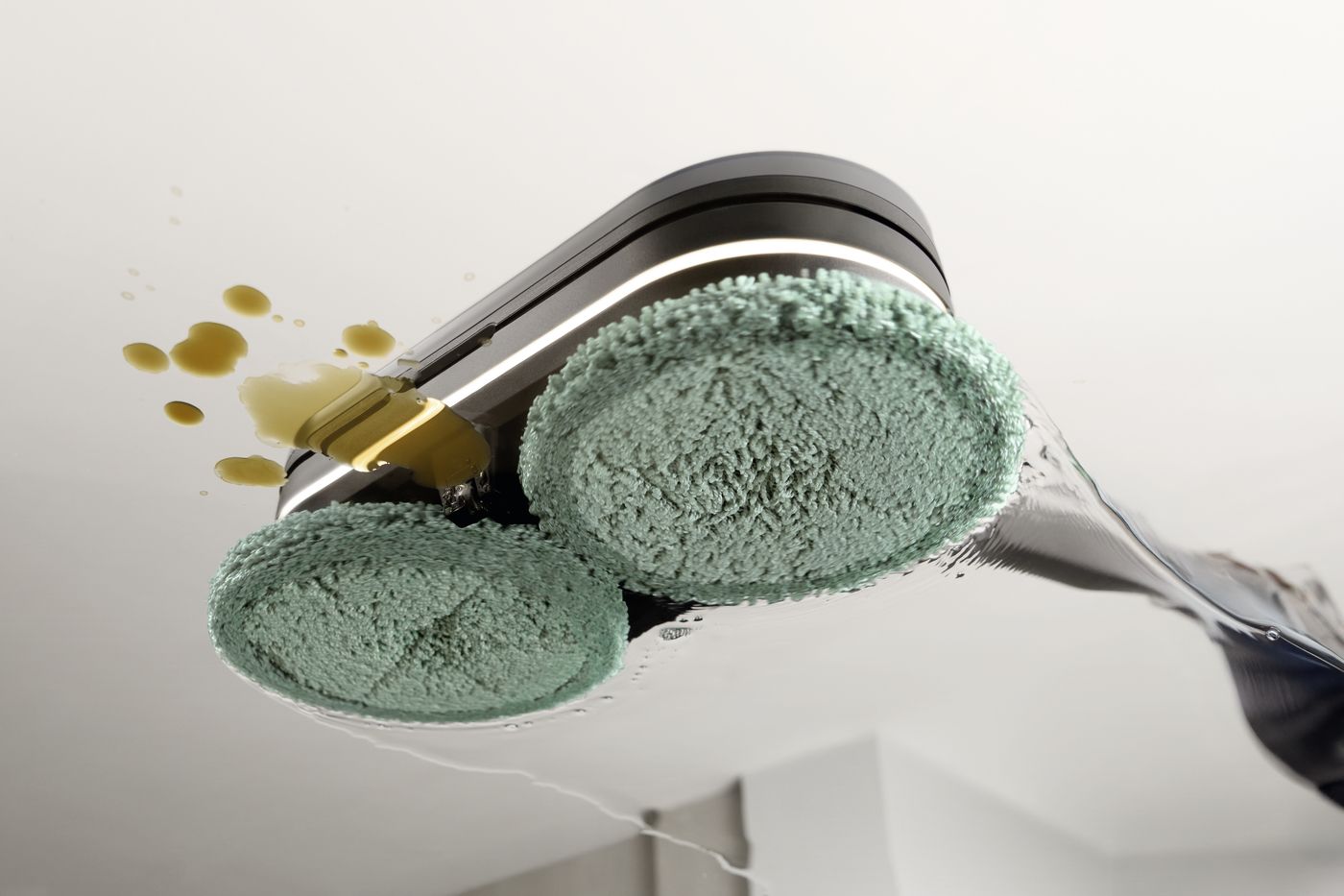 Close-up of a ceiling cleaning tool with two green sponge pads and a yellow cleaning liquid splash on the ceiling surface.