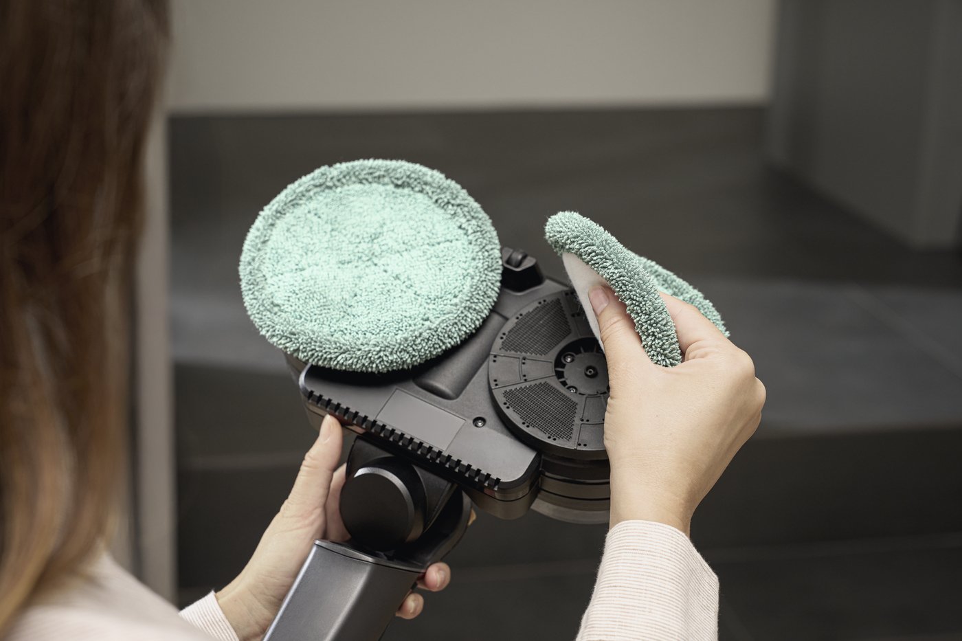 Close-up of a person cleaning a round green microfiber pad on a handheld floor buffer.