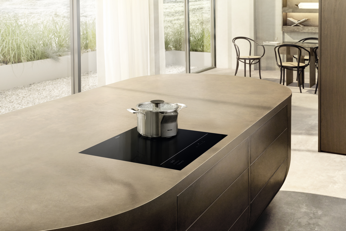 Modern kitchen island with a built-in induction cooktop and a stainless steel pot, in a bright, open room with glass walls.